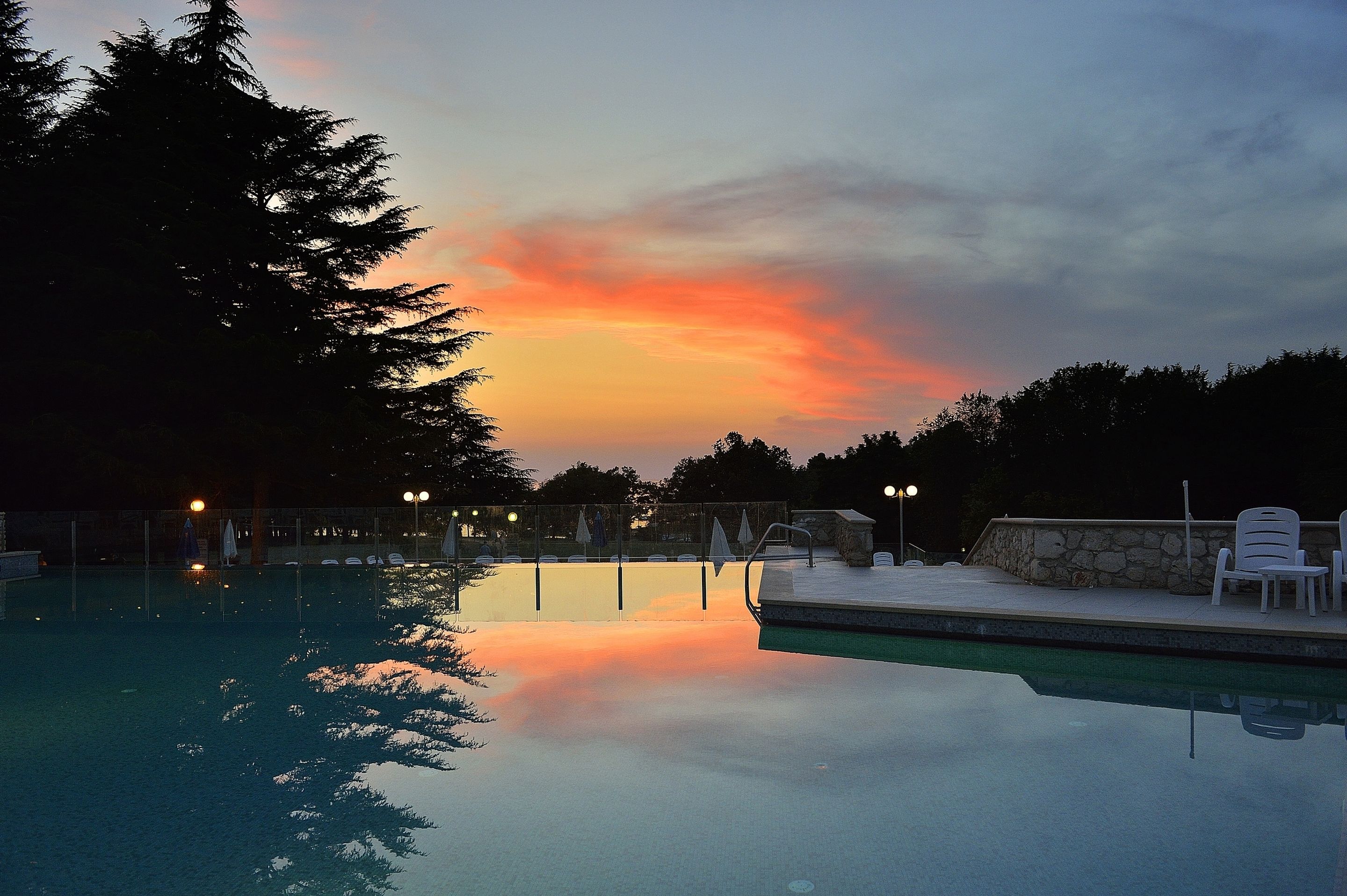 A swimming pool with a sunset view, surrounded by trees and equipped with lounge chairs.