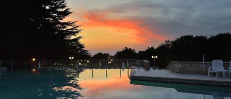 A swimming pool with a sunset view, surrounded by trees and equipped with lounge chairs.