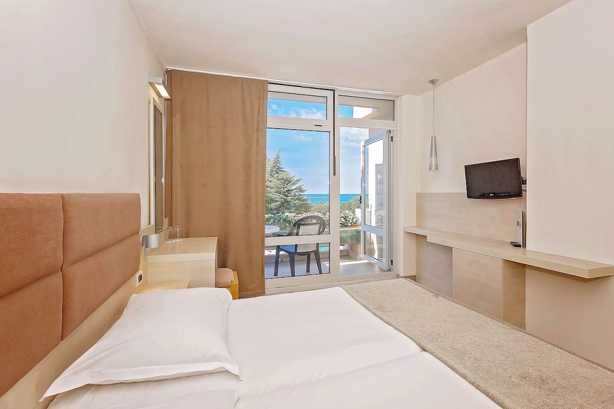 A hotel room with a bed, a TV, a desk, and a view of the outdoors.