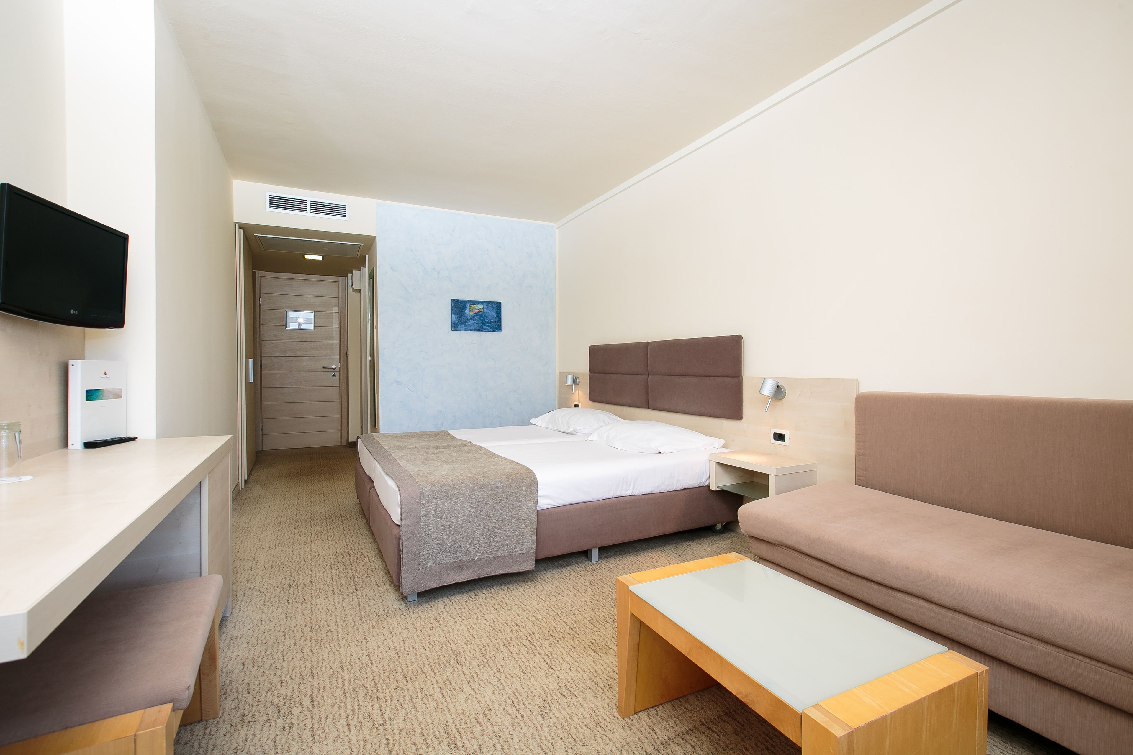A hotel room with a bed, a sofa, a desk, and a TV.