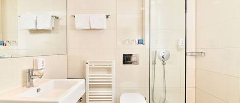 A modern bathroom with a white sink, a toilet, a glass shower enclosure, and a towel rack with two towels.