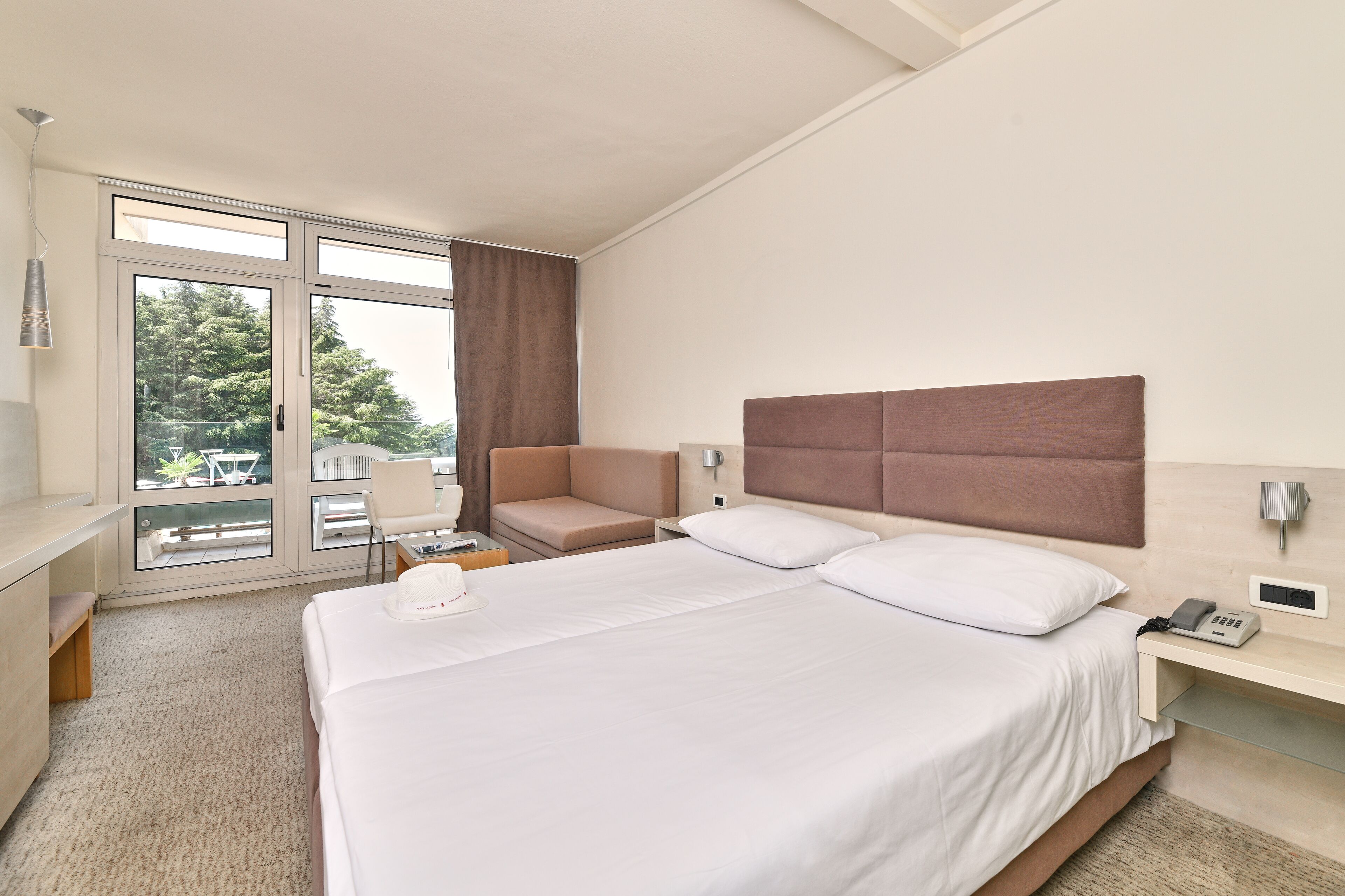 A hotel room with a large bed, a desk, a chair, and a view of the outdoors.