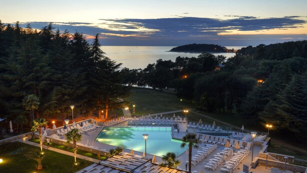 Ein Resort mit großem Pool, Liegestühlen und Blick auf das Meer im Abenddämmerung.