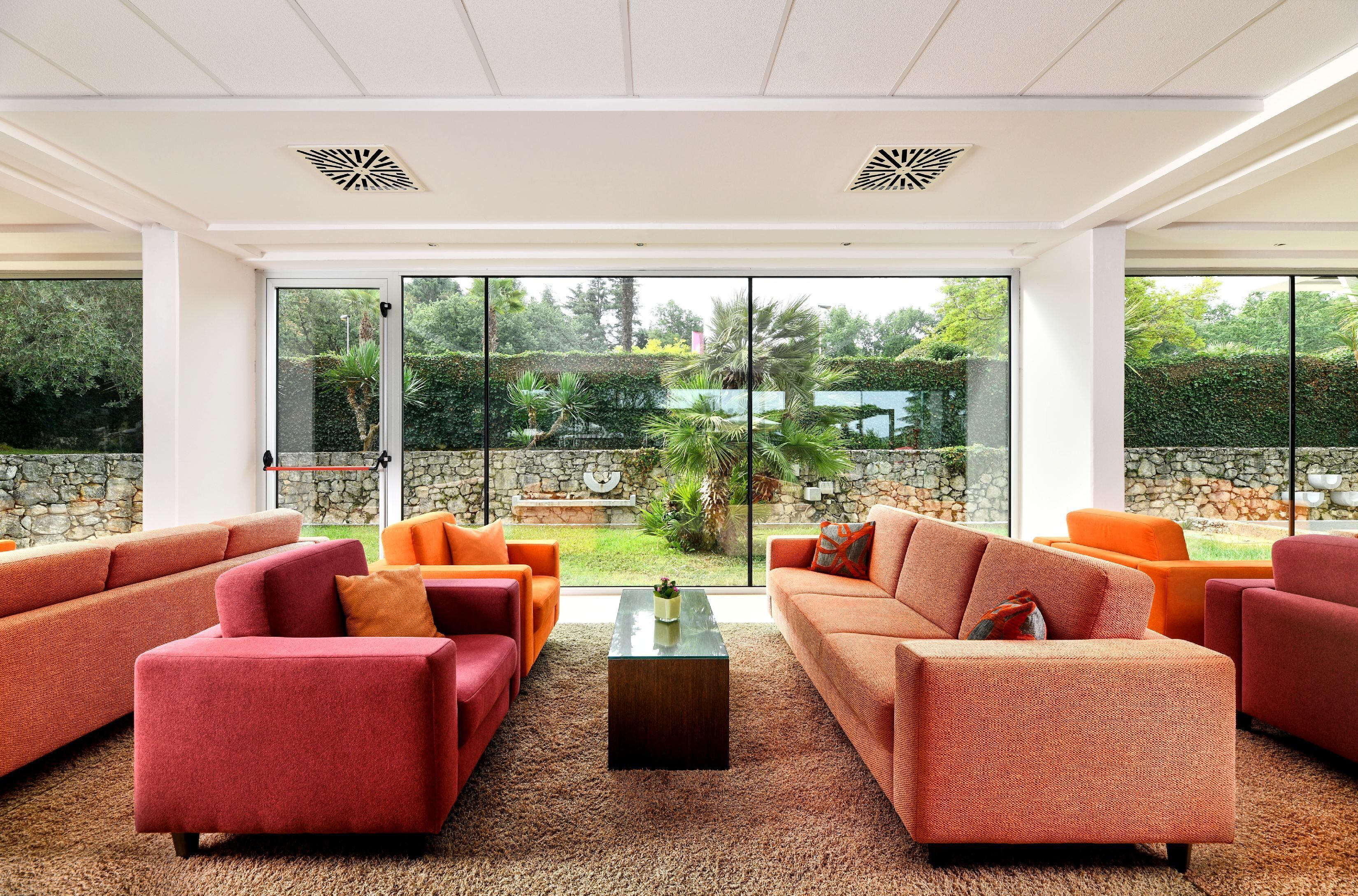 Ein modernes Wohnzimmer mit großen Fenstern, roten Sofas und einem zentralen Couchtisch.