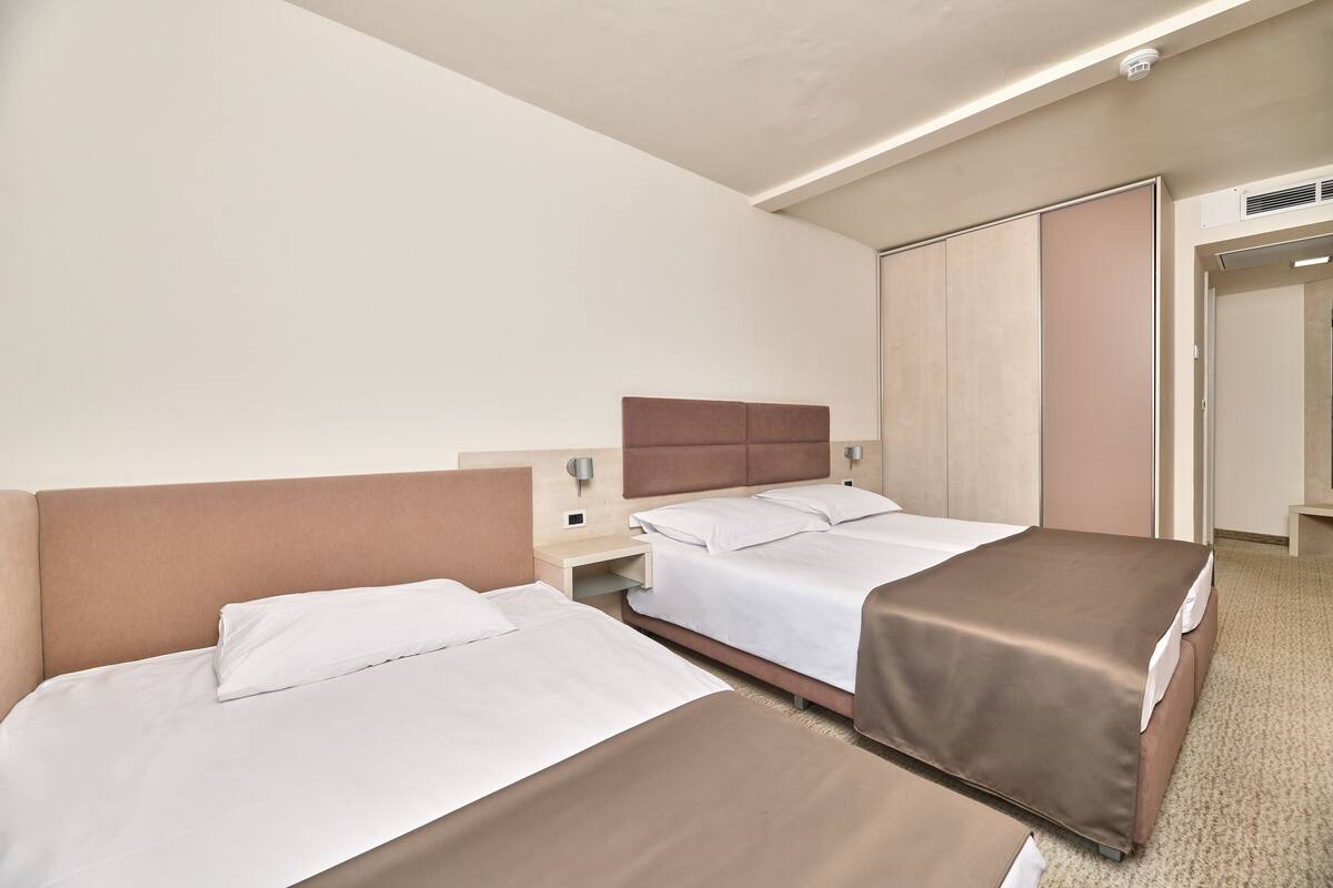 A hotel room with two beds, a wardrobe, and a bathroom.