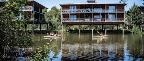 A wooden multi-story building with a balcony, situated over a body of water.