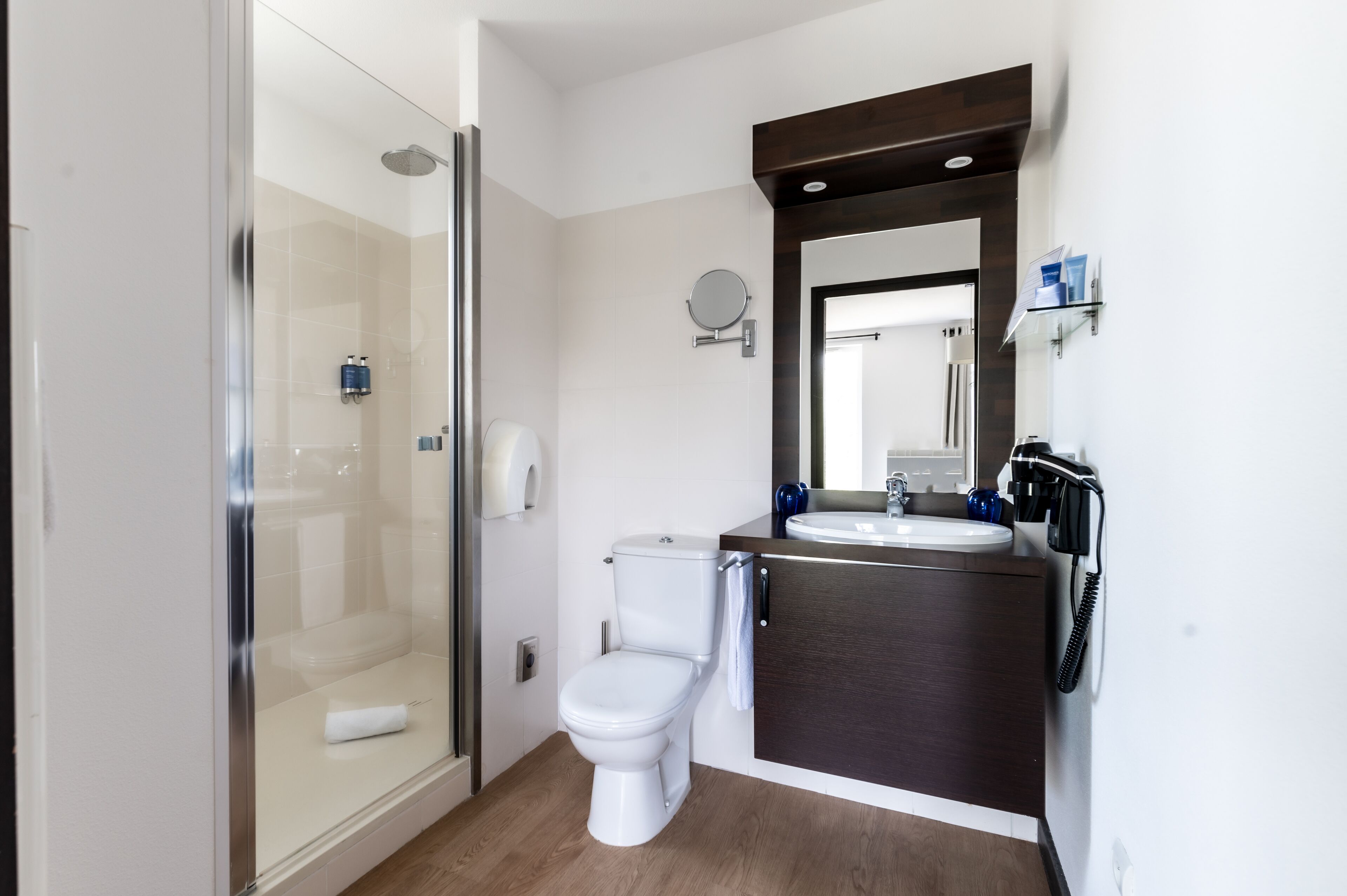 A modern bathroom with a glass shower enclosure, a white toilet, a dark wood vanity with a mirror, and a sink.