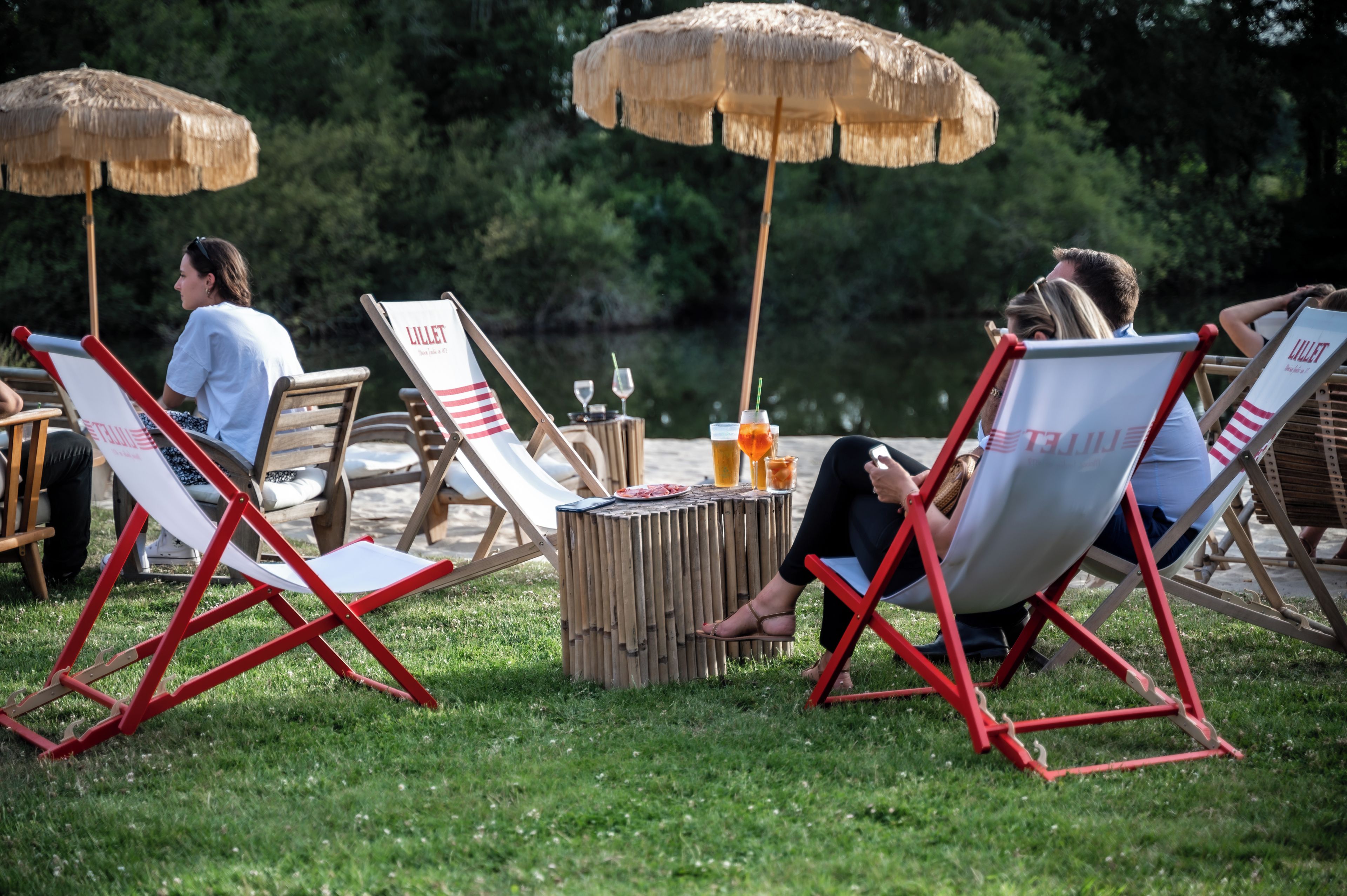 Mobiliario exterior con sombrillas, una mesa con bebidas y un lago al fondo.