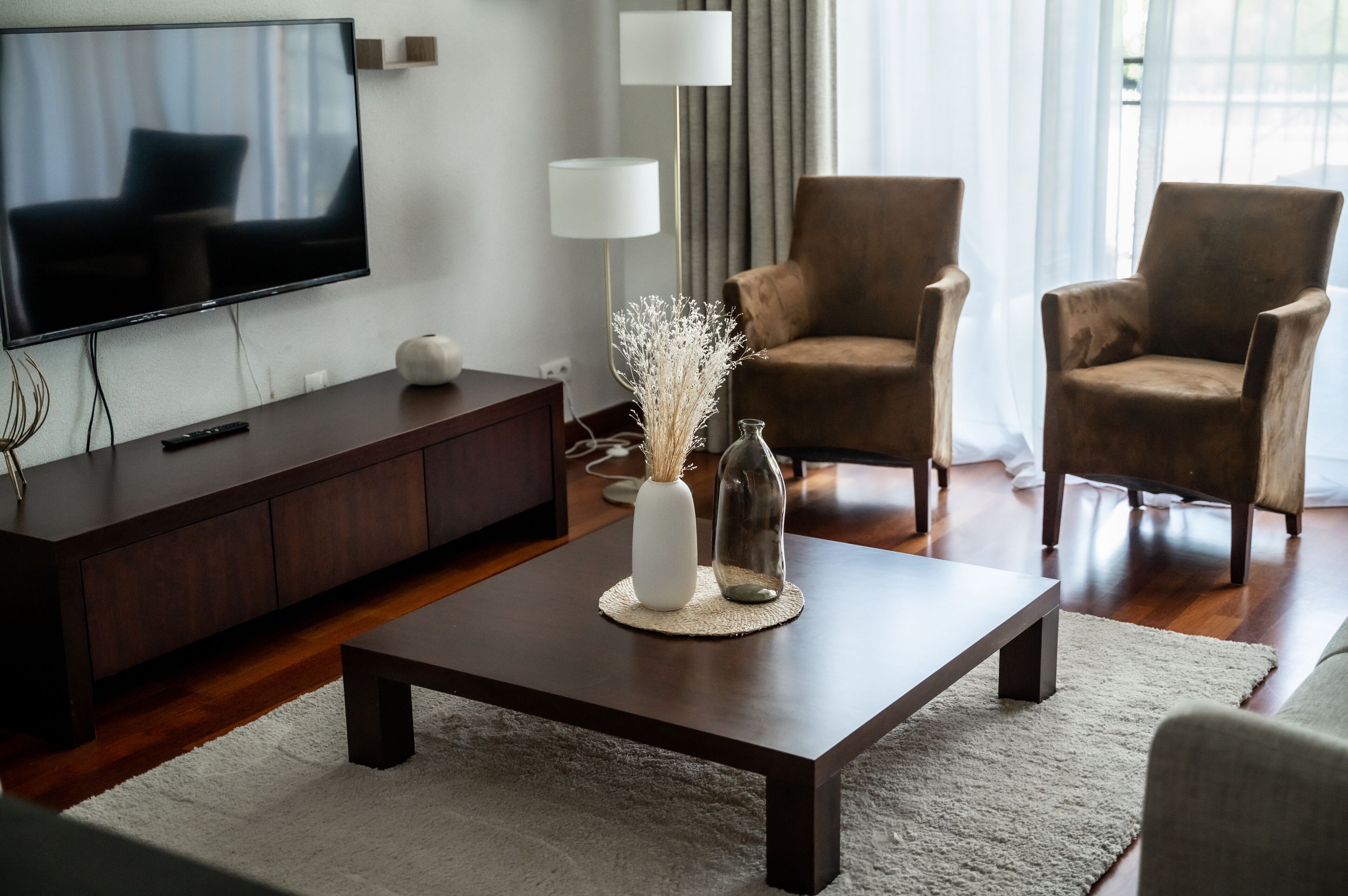 Uma sala de estar moderna com televisão de tela plana, móveis de madeira escura e um vaso decorativo sobre uma mesa de centro.