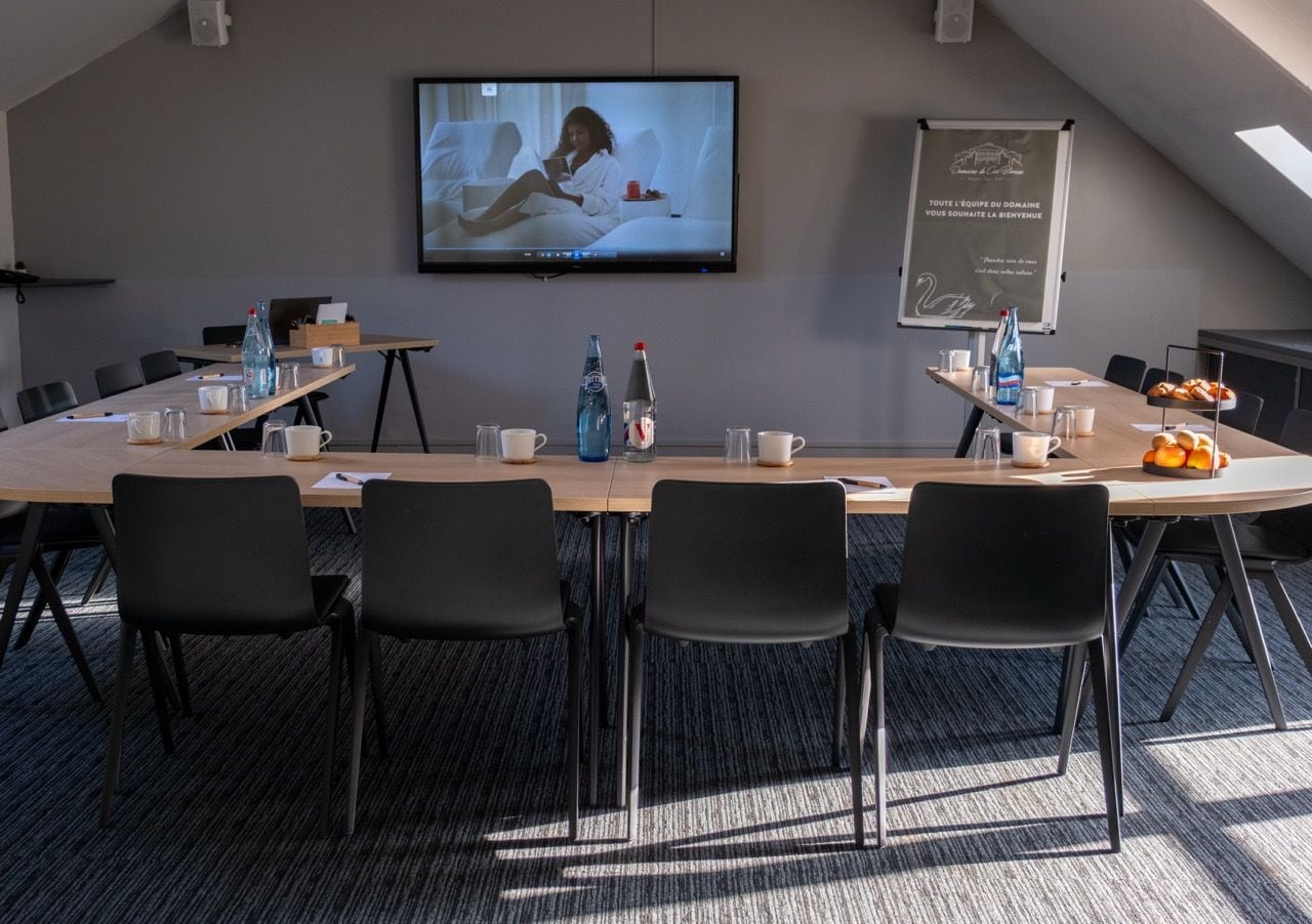 A conference room with a long table, black chairs, a television screen, and a projection screen.