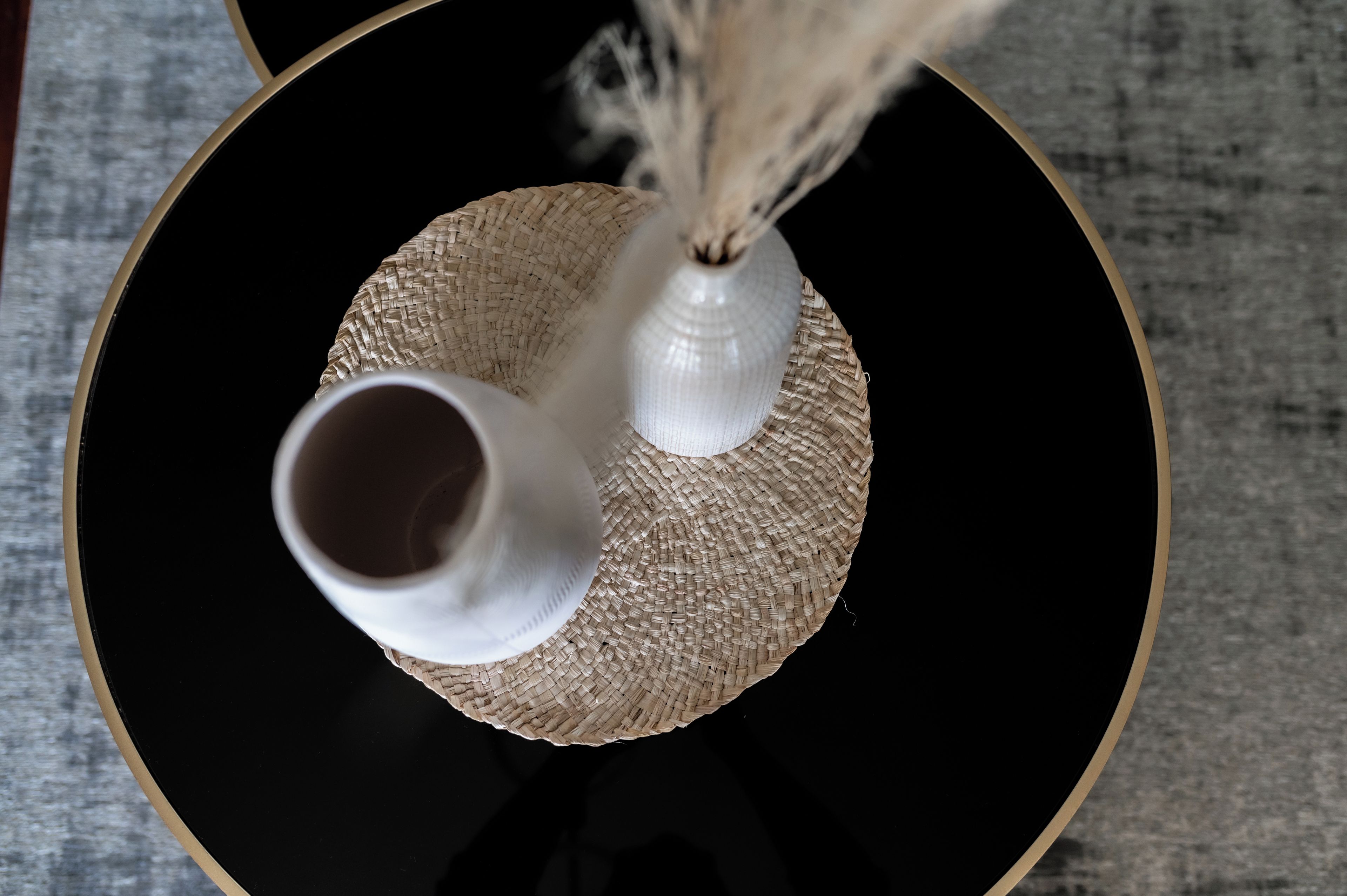 A black table with two white vases on a woven placemat.