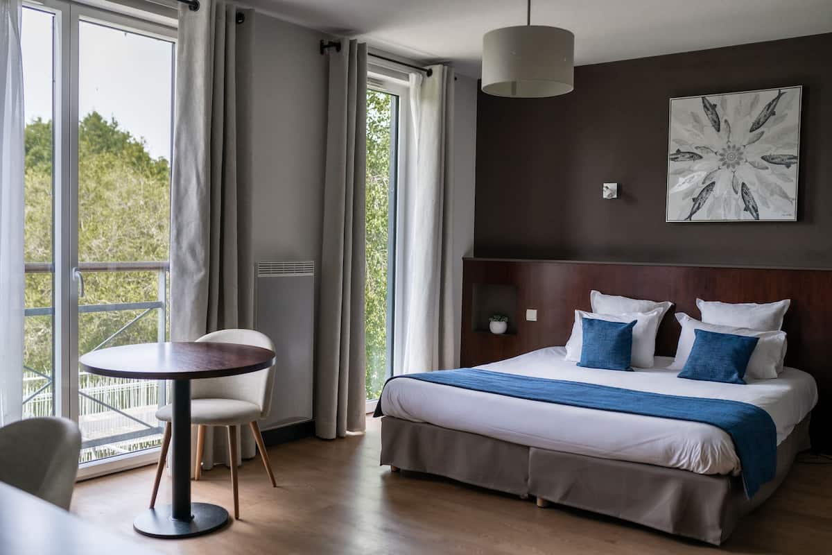A hotel room with a bed, a round table, a chair, and a balcony with a railing.