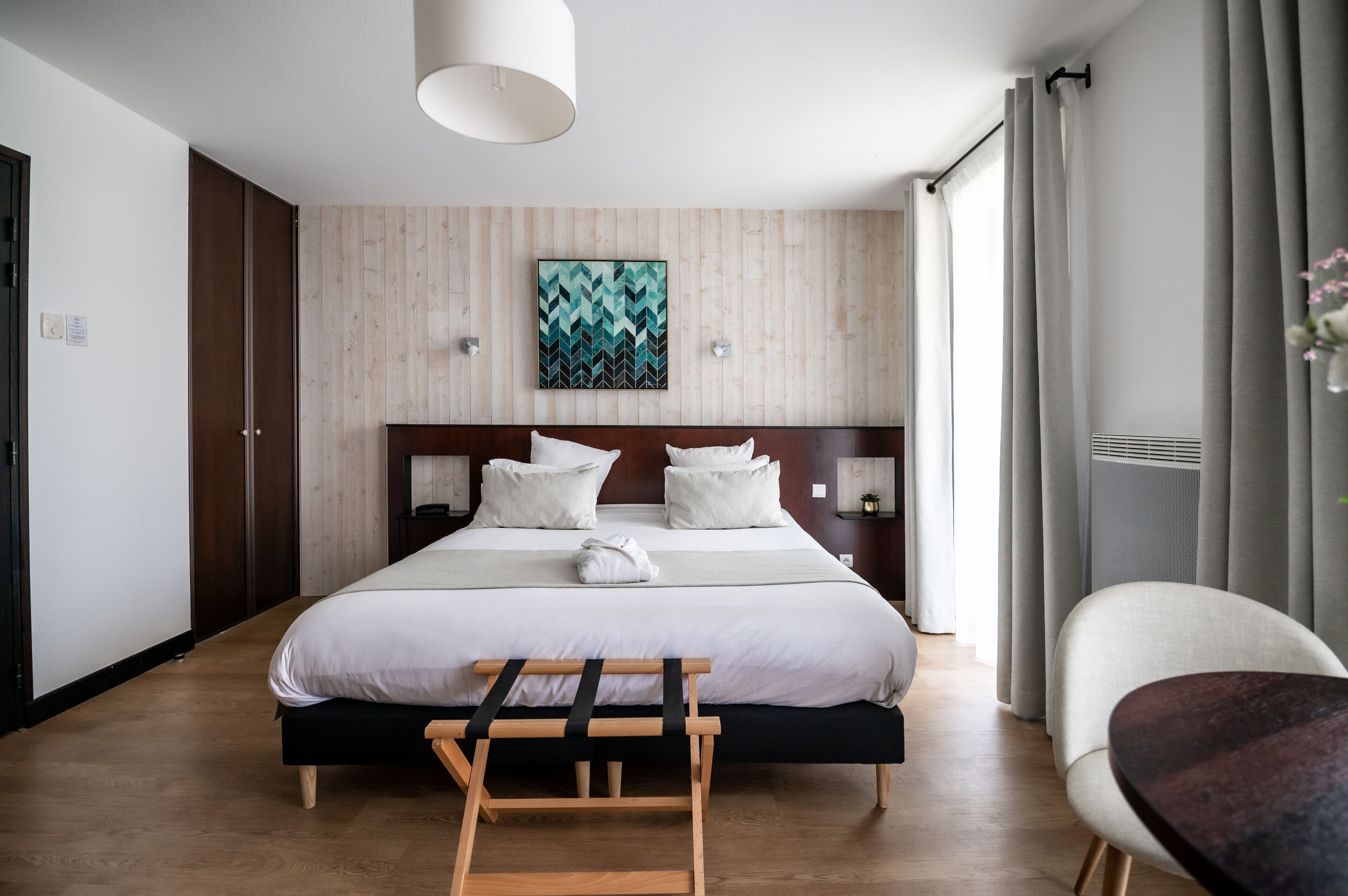 Ein Hotelzimmer mit einem großen Bett, einem Holzkopfstück, Nachttischen, einer Bank und einem Sessel.