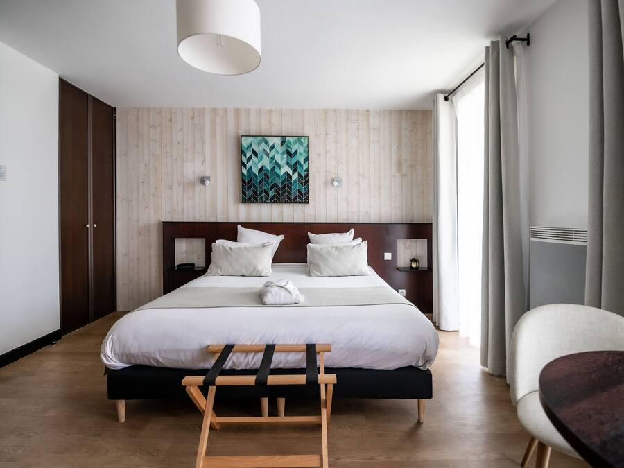 Ein Hotelzimmer mit einem großen Bett, einem Holzkopfstück, Nachttischen, einer Bank und einem Sessel.