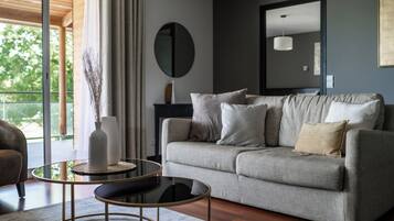 Una sala de estar moderna con un sofá gris, una mesa redonda de centro y un amplio ventanal con cortinas.