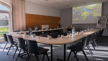 Un salón de conferencias con una larga mesa, sillas, una pantalla de proyector y una pizarra para presentaciones.