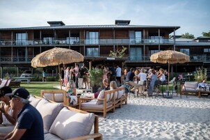 Hotel frente al mar con mesas y sombrillas al aire libre, zona de bar y un cartel que dice 'La Paillotte'.
