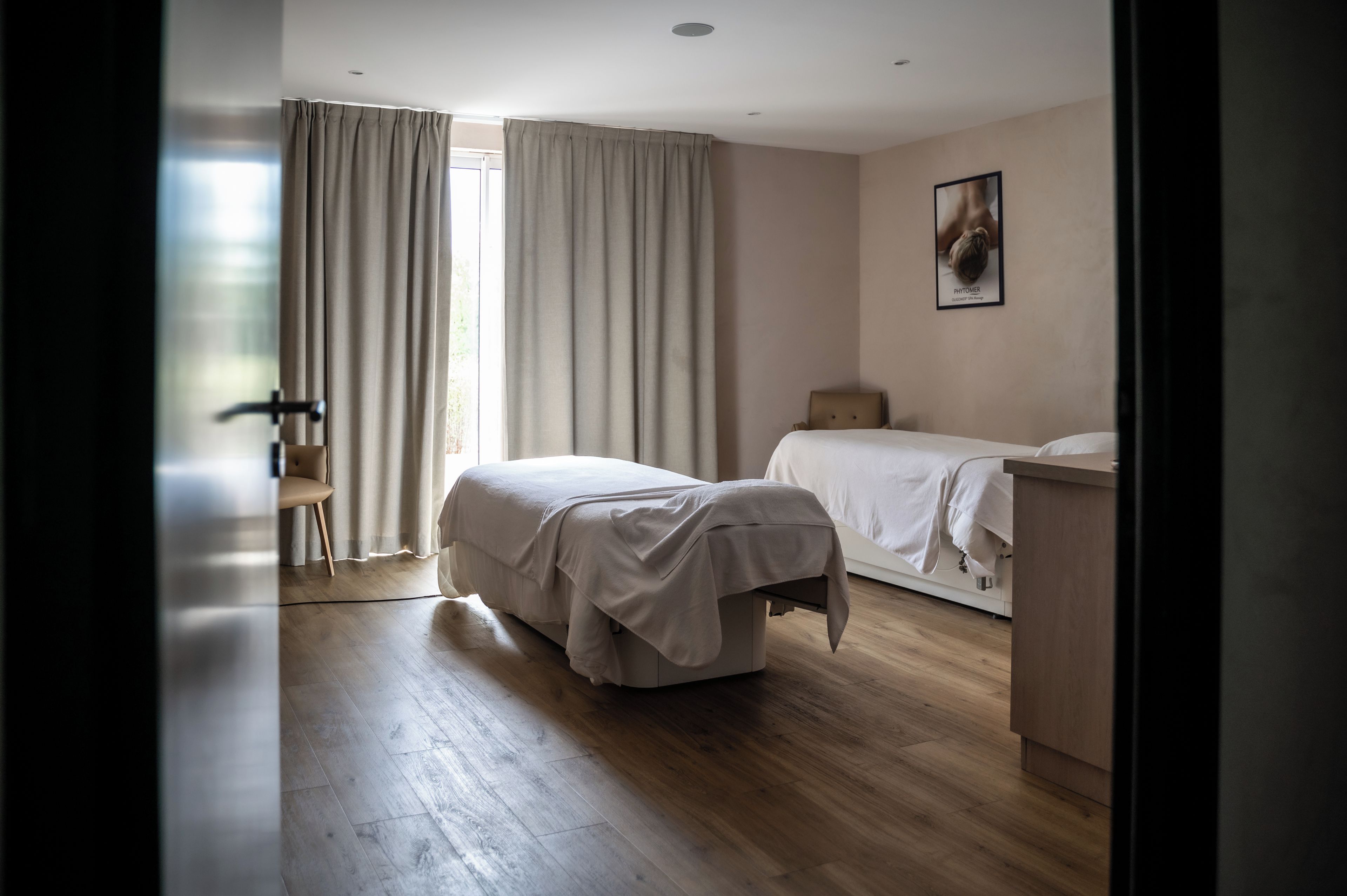 A bedroom with a single bed, a chair, a bedside table, and a window with curtains.