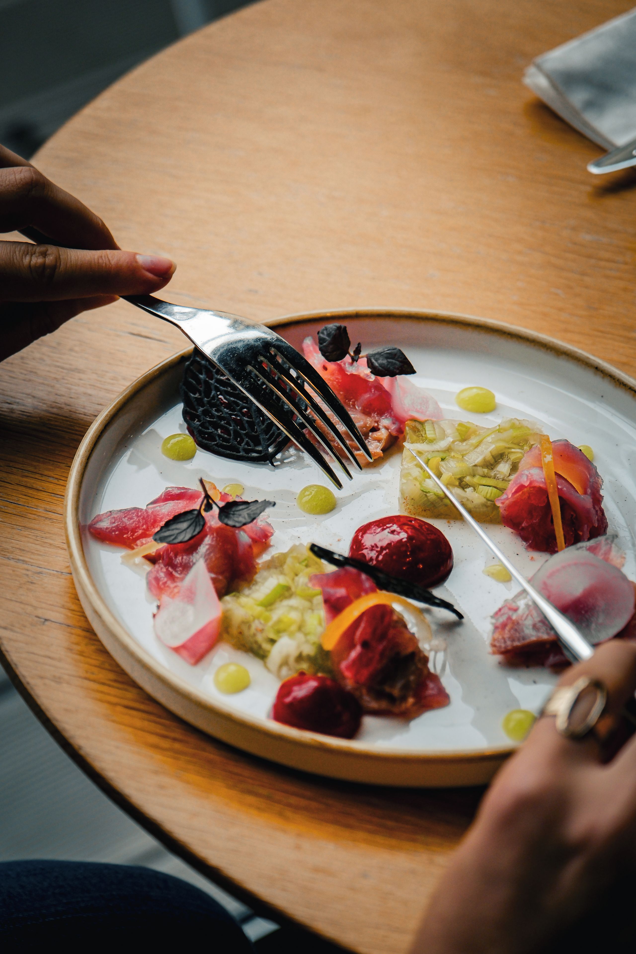 A plate of food with various items including a black item, red slices, and green elements, accompanied by a fork.