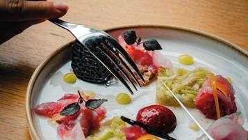 A plate of food with various items including a black item, red slices, and green elements, accompanied by a fork.
