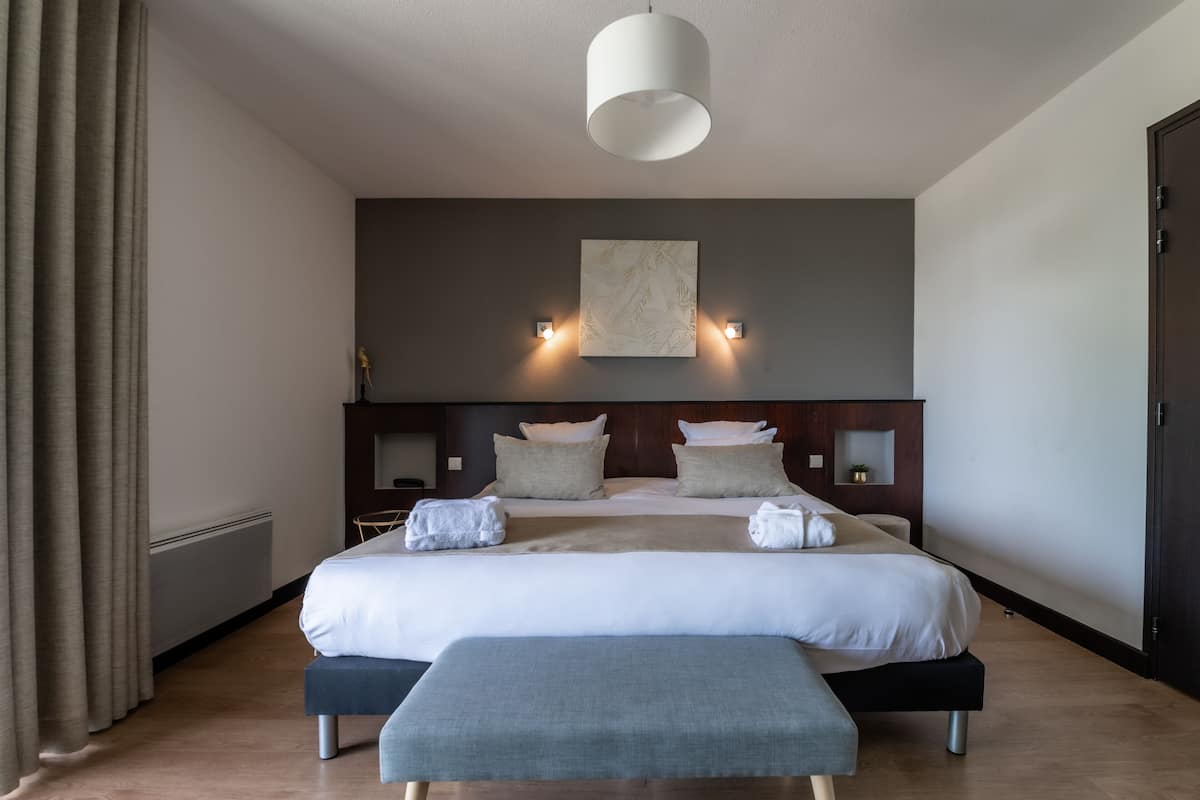 A modern hotel room with a large bed, bedside tables, a bench, and a ceiling light.