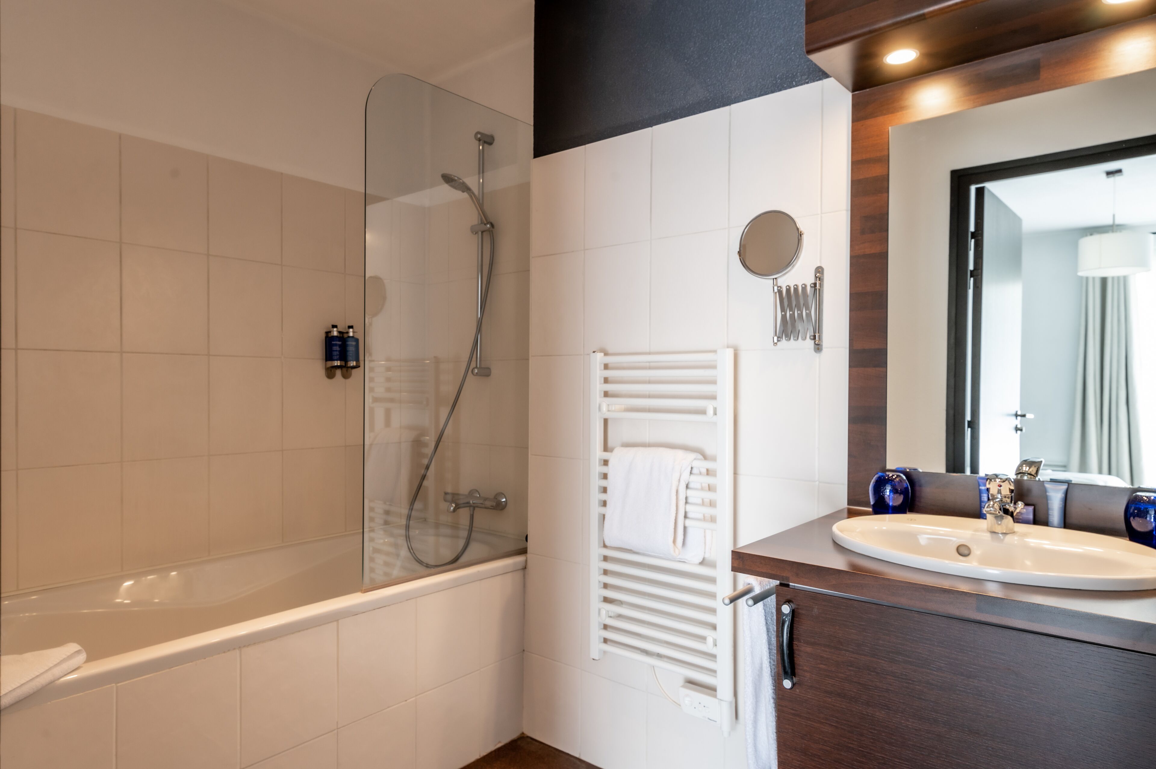 Ein modernes Badezimmer mit einer Badewanne, einer Duschkabine, einem weißen Handtuchhalter, einem Waschbecken mit Spiegel und einem Handtuch am Halter.