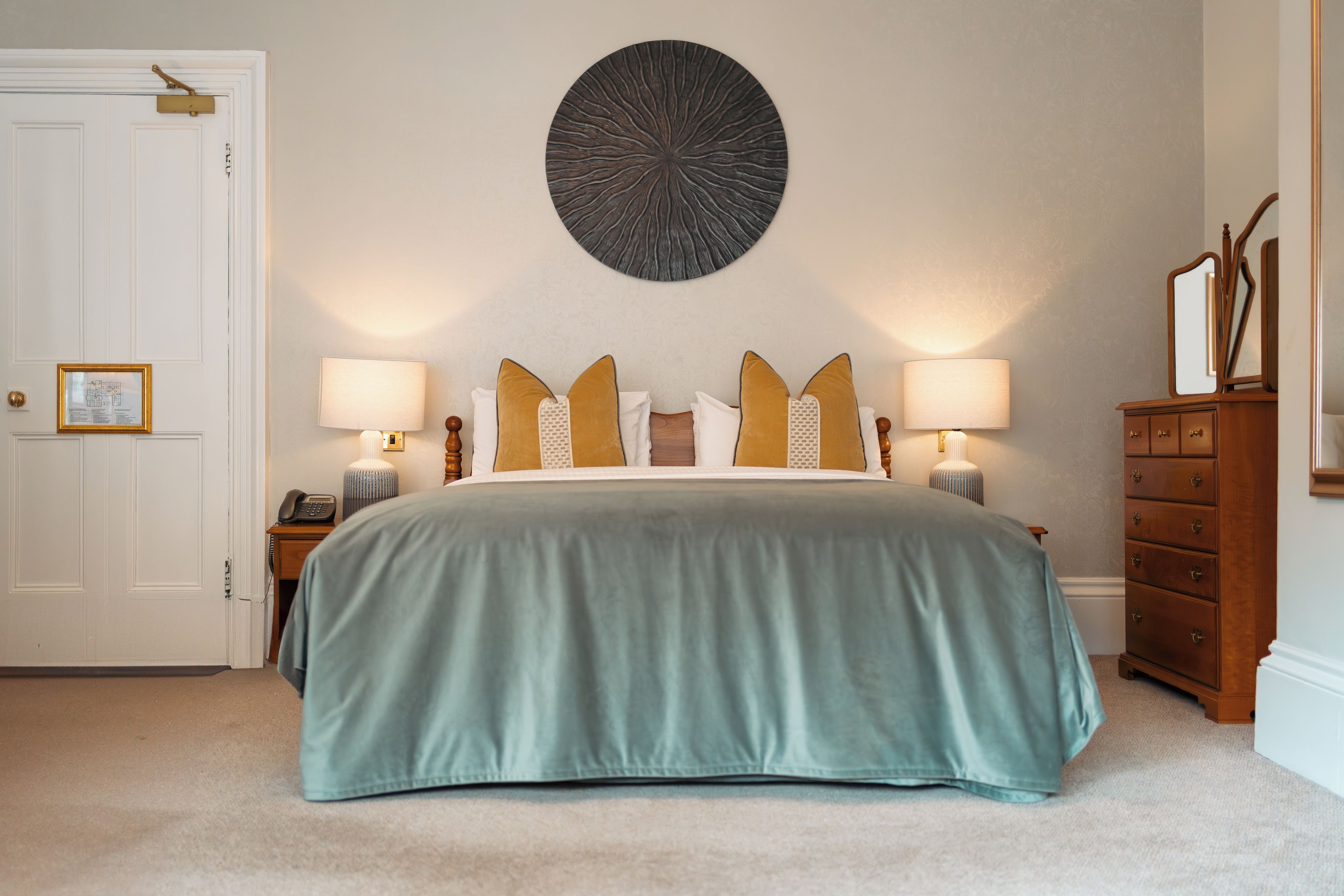 A bedroom with a bed, two bedside tables, a nightstand, a dresser, a mirror, and a wall-mounted decorative piece.