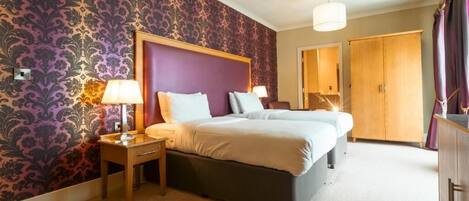 A bedroom with a large bed, two bedside tables with lamps, a wardrobe, and a patterned wallpaper.