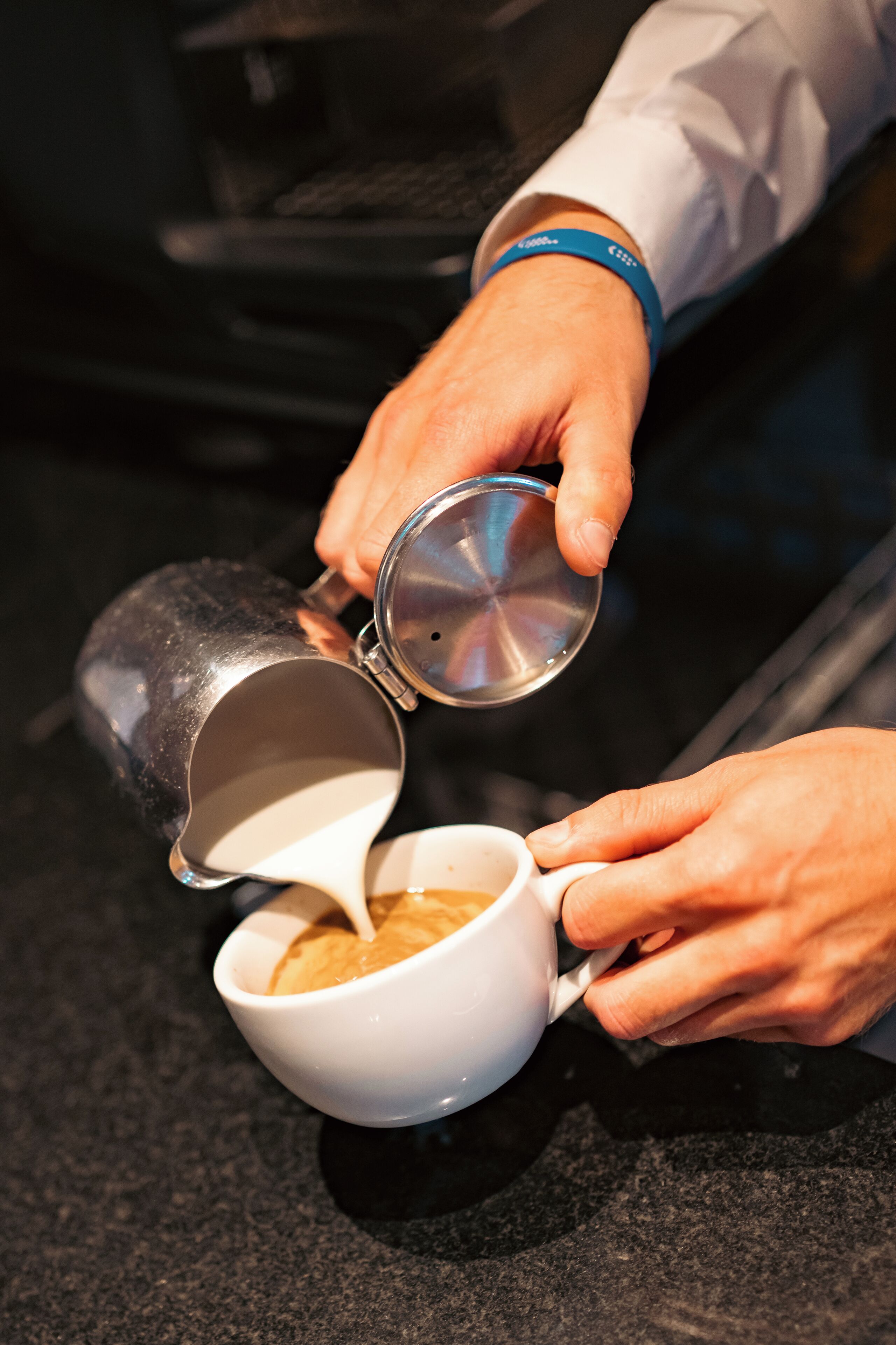 A person pouring coffee from a metal pot into a white cup.