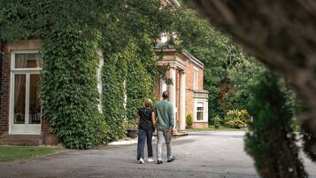 Un couple se tient devant un bâtiment à la façade en briques et aux colonnes, entouré de verdure.