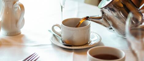 A table with a teapot pouring tea into a cup, a glass of water, and a fork on a napkin.