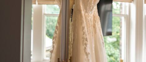 Un vestido de novia colgado de una percha en una habitación con ventanas amplias.