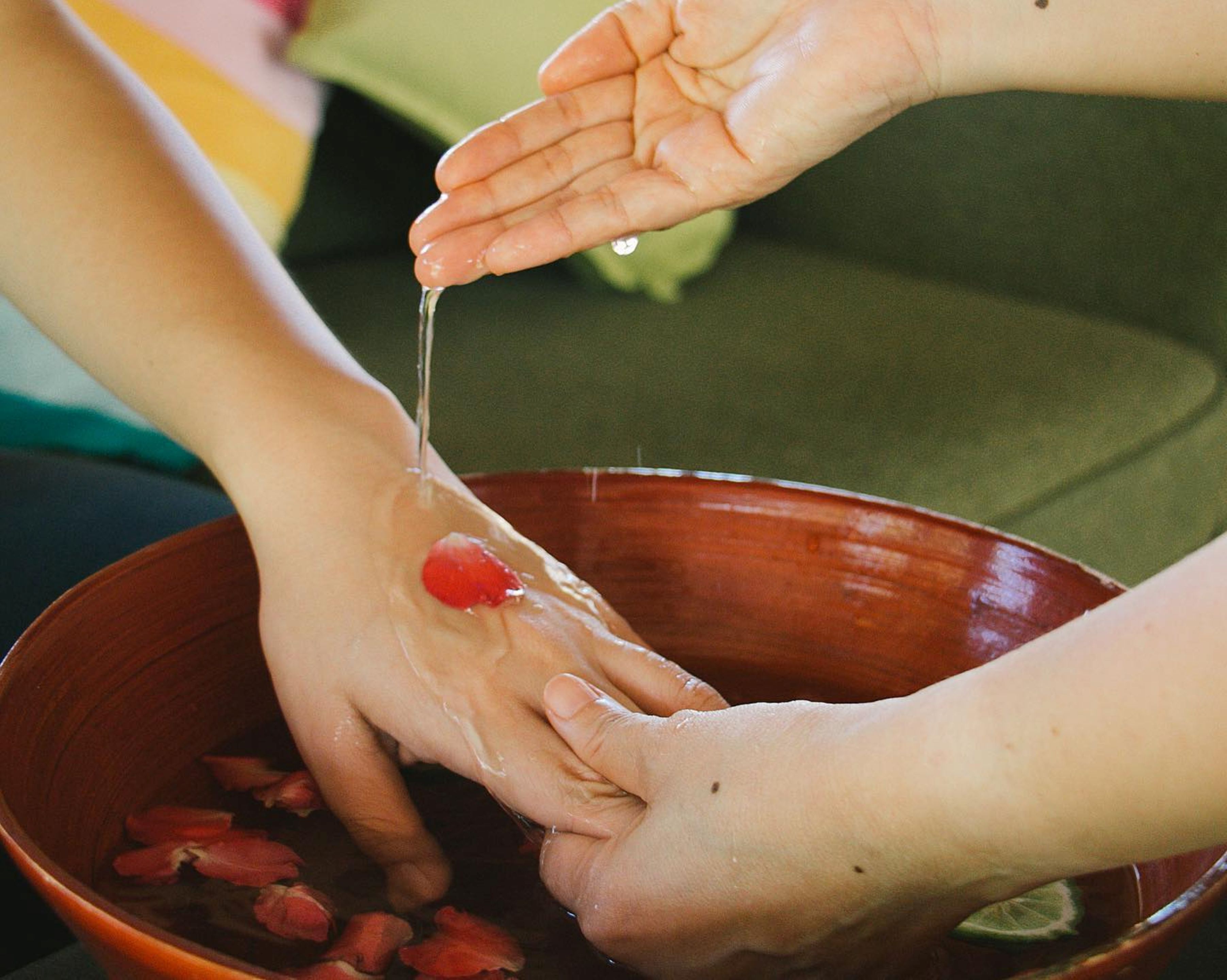 A person washing hands in a bowl with rose petals.