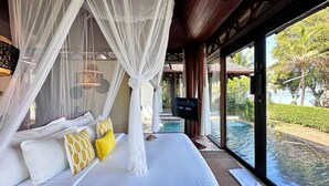 A bedroom with a large bed, white and yellow pillows, a TV, and a view of a pool and greenery. - The Vijitt Resort Phuket (Rawai)
