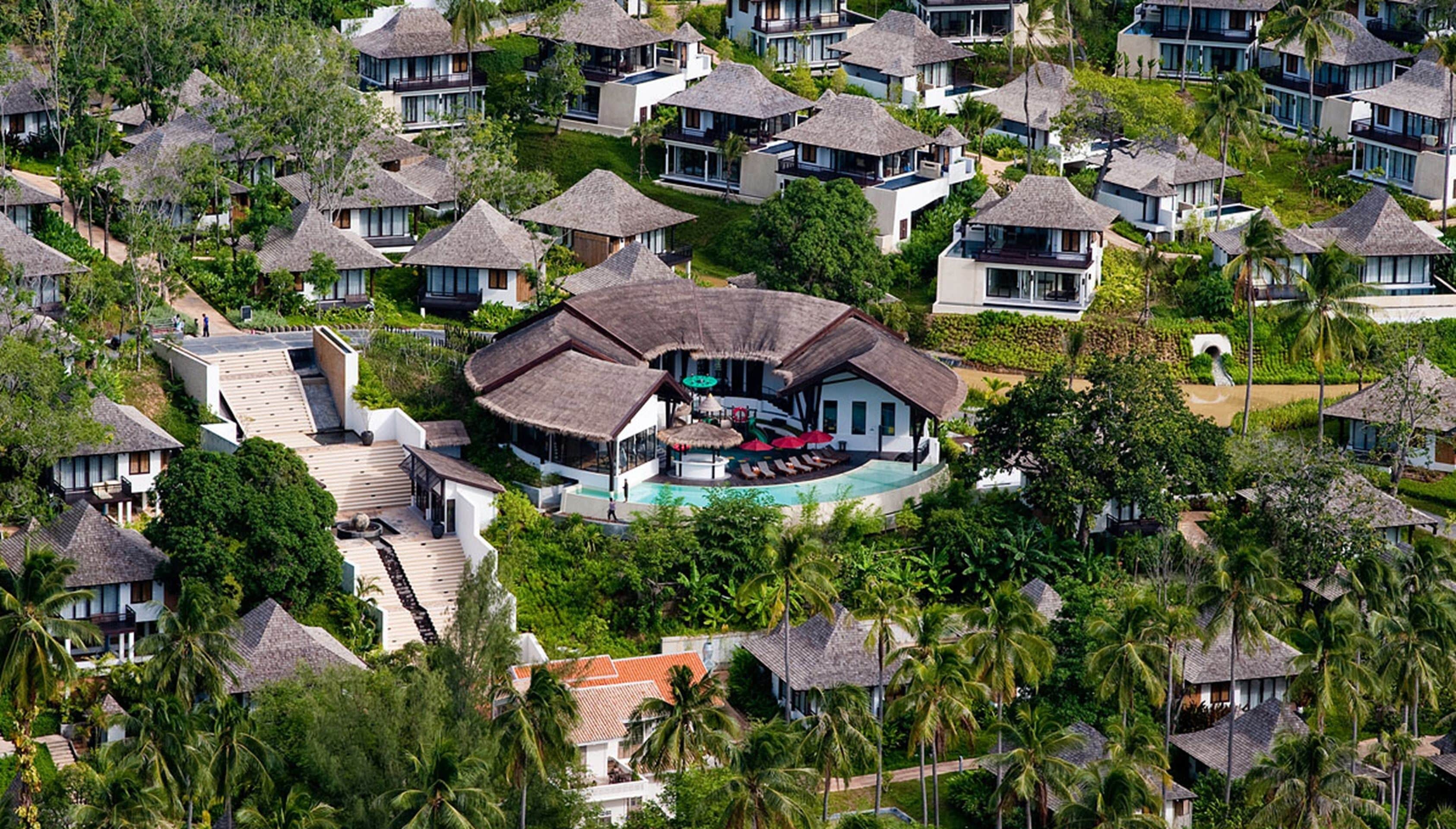 Ein Resort mit mehreren bungalowartigen Gebäuden, einem zentralen kreisförmigen Gebäude mit Pool, umgeben von üppiger Vegetation und Palmen.