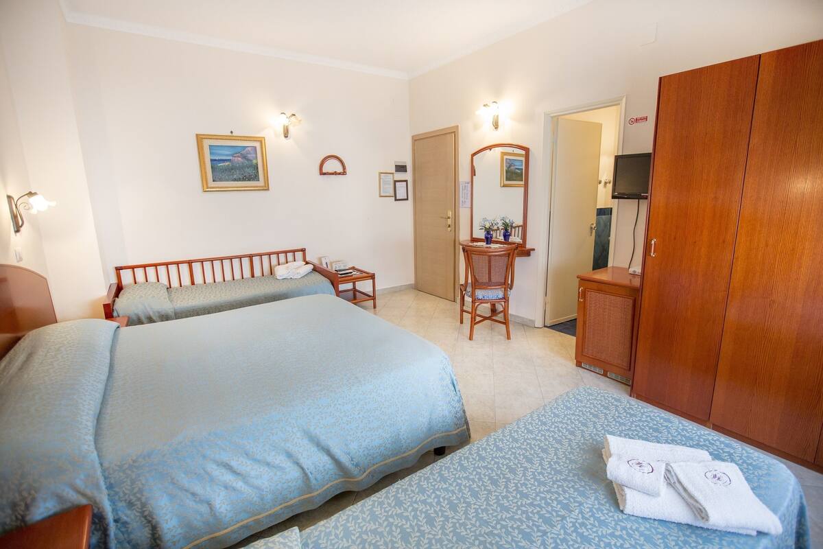 A hotel room with two beds, a wooden wardrobe, a television, and a bathroom visible through an open door.