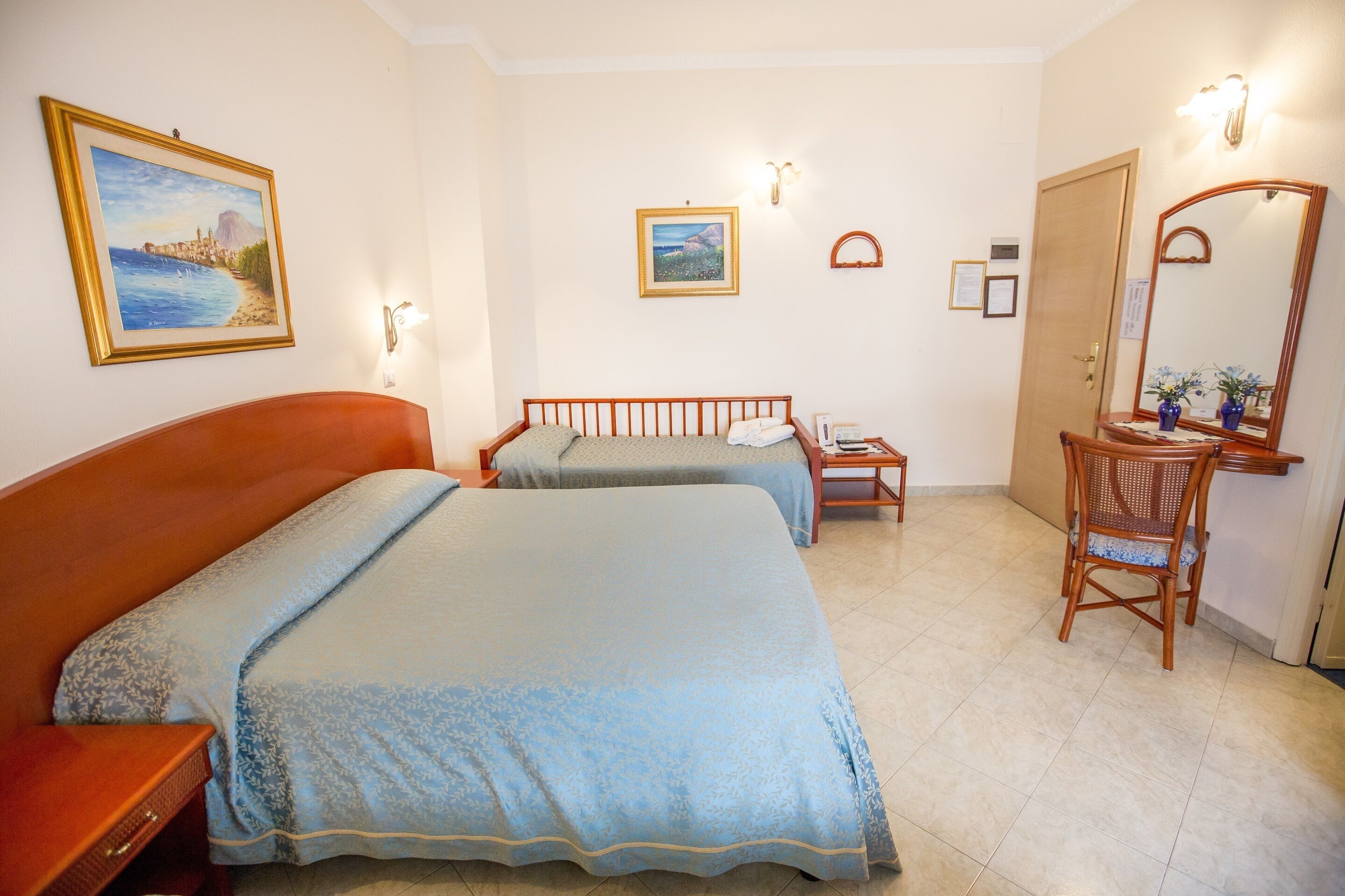 A hotel room with two beds, a wooden chair, a desk, and a large mirror.