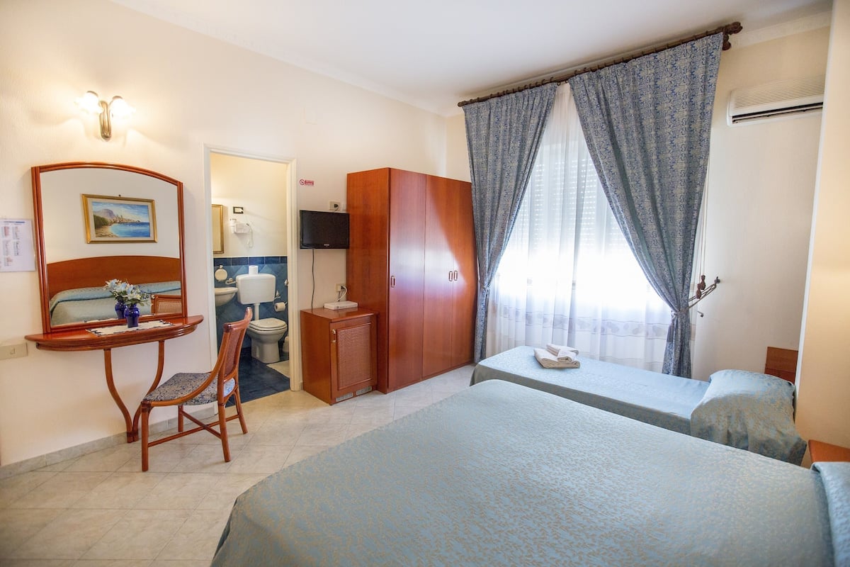 A hotel room with two beds, a desk with a chair, a wardrobe, a bathroom with a toilet and sink, and a television mounted on the wall.