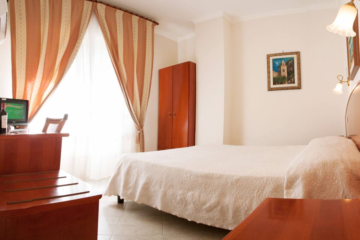 A hotel room with a bed, a wooden desk, a computer, and a wardrobe.