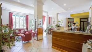 A spacious lobby with a reception desk, seating area with sofas and chairs, and potted plants. - Mediterraneo (Cefalù)