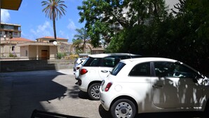 A parking area with white cars, a palm tree, and buildings in the background. - Mediterraneo (Cefalù)