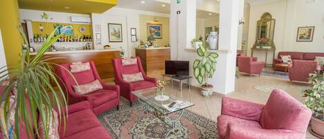 A hotel lobby with red armchairs, a reception desk, and a bar area.