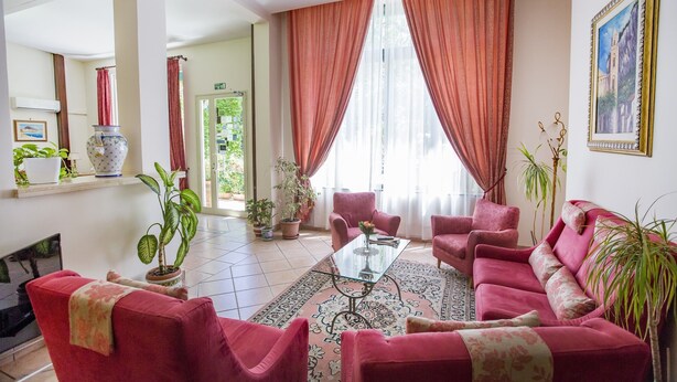 A living room with red sofas, a glass coffee table, and potted plants. - Mediterraneo (Cefalù)