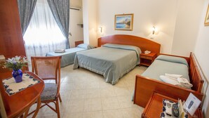 A hotel room with two beds, a dining table with a vase, a chair, a small table with a remote control, and a painting on the wall. - Mediterraneo (Cefalù)