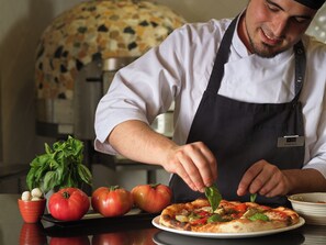 Un chef preparando una pizza con tomates y albahaca sobre una encimera.