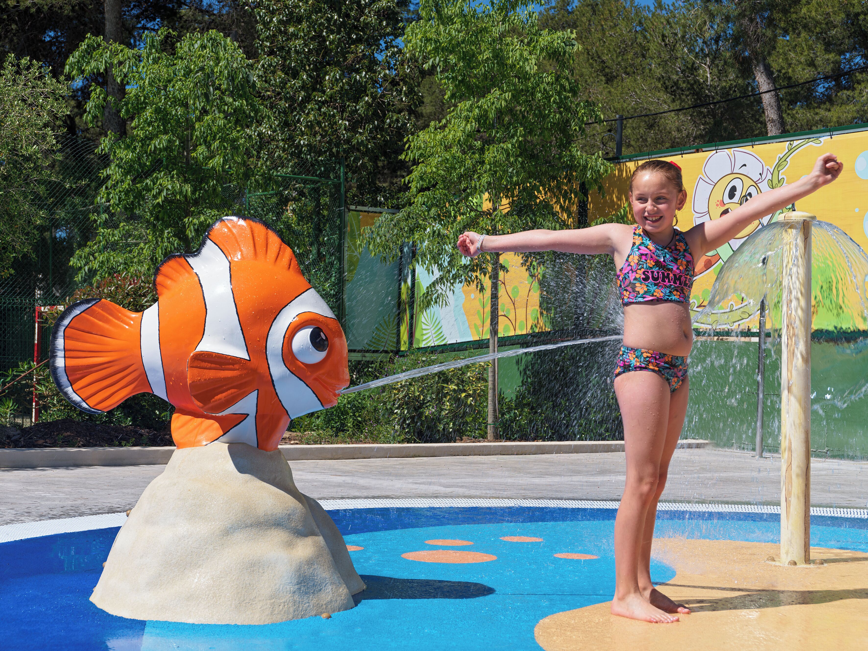 Niño jugando con una fuente con forma de pez payaso en una piscina.