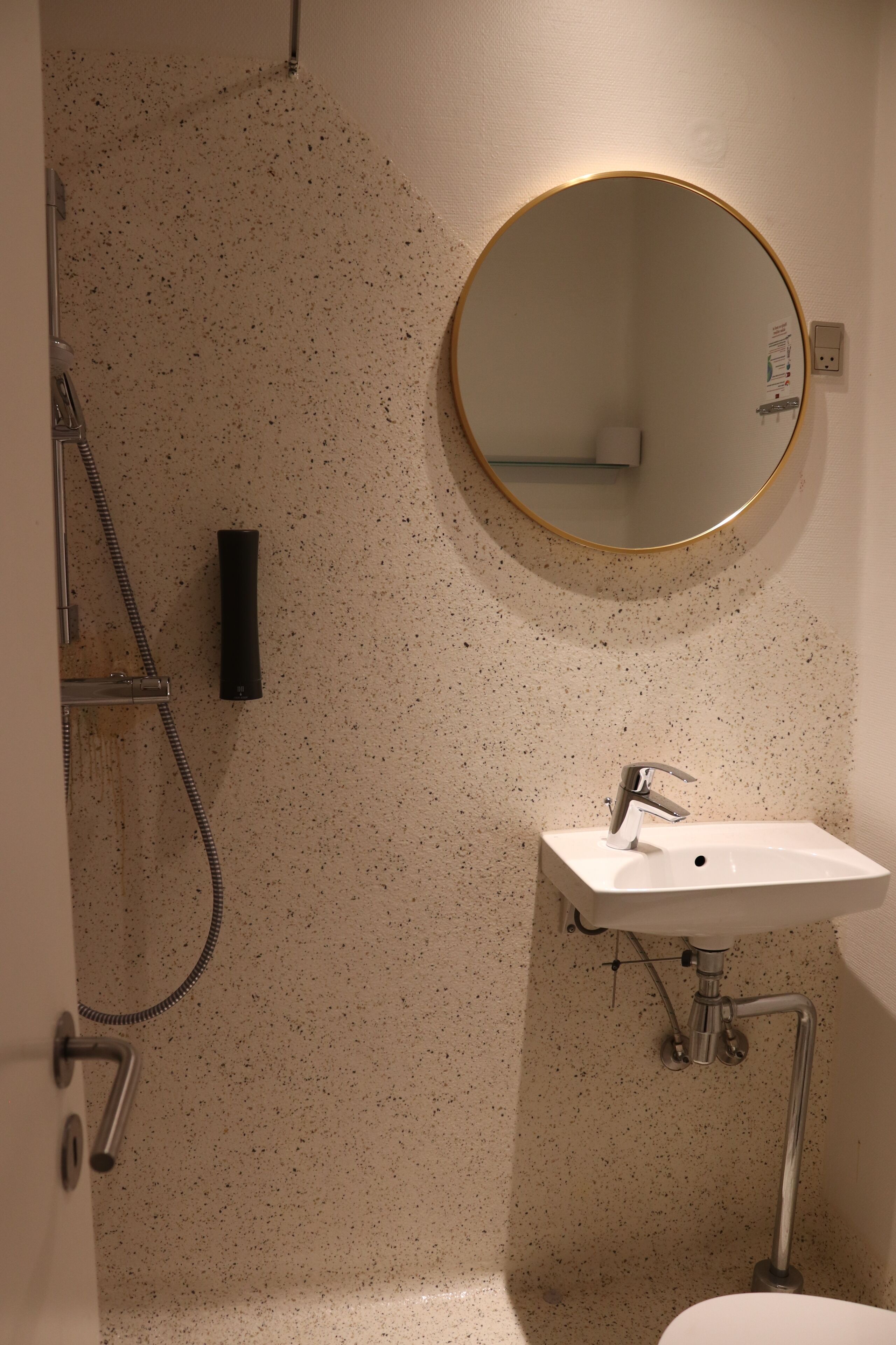 Un baño con lavamanos blanco, un espejo redondo y una ducha.