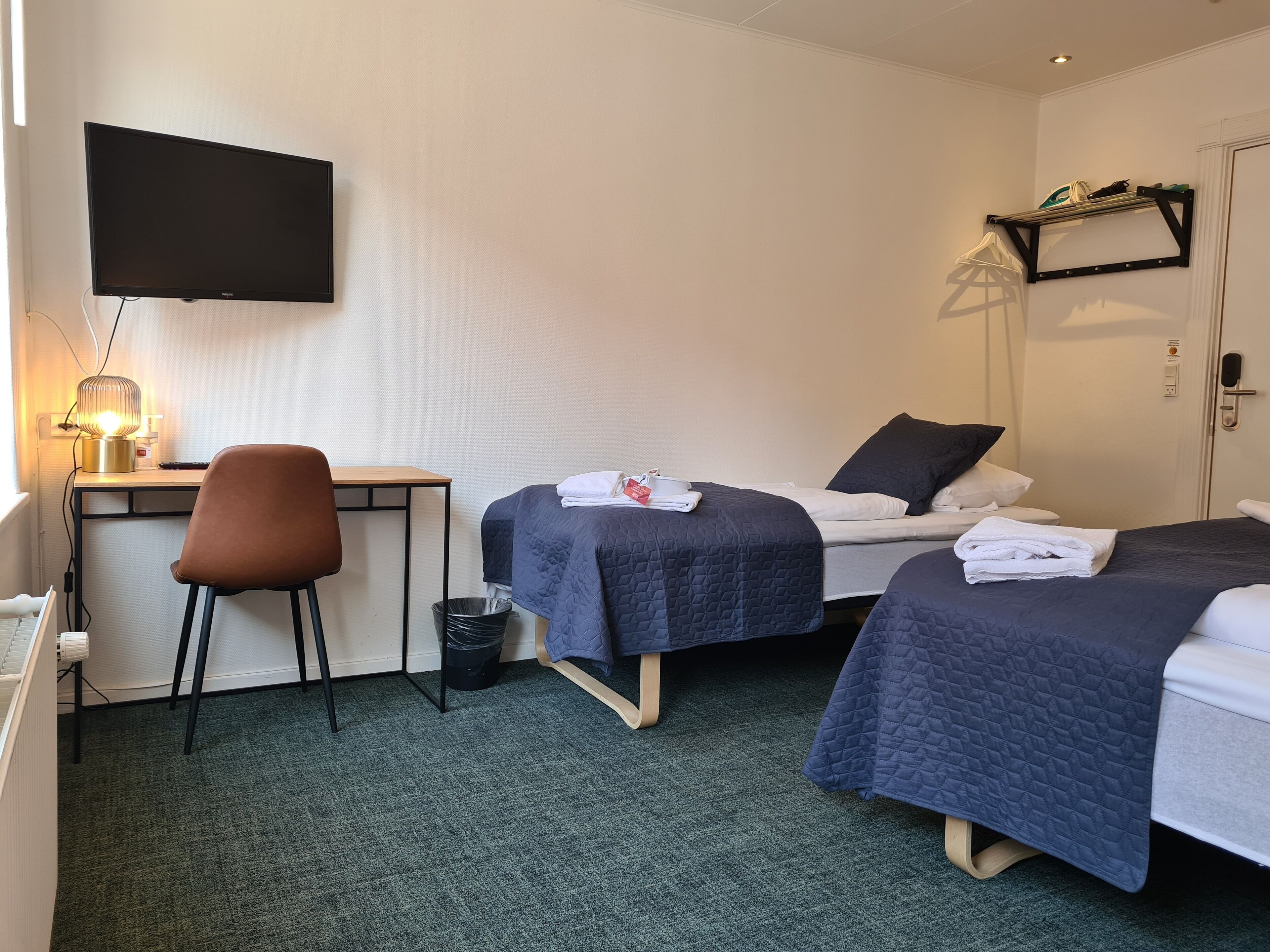 A hotel room with two beds, a desk, a chair, a TV, and a trash bin.