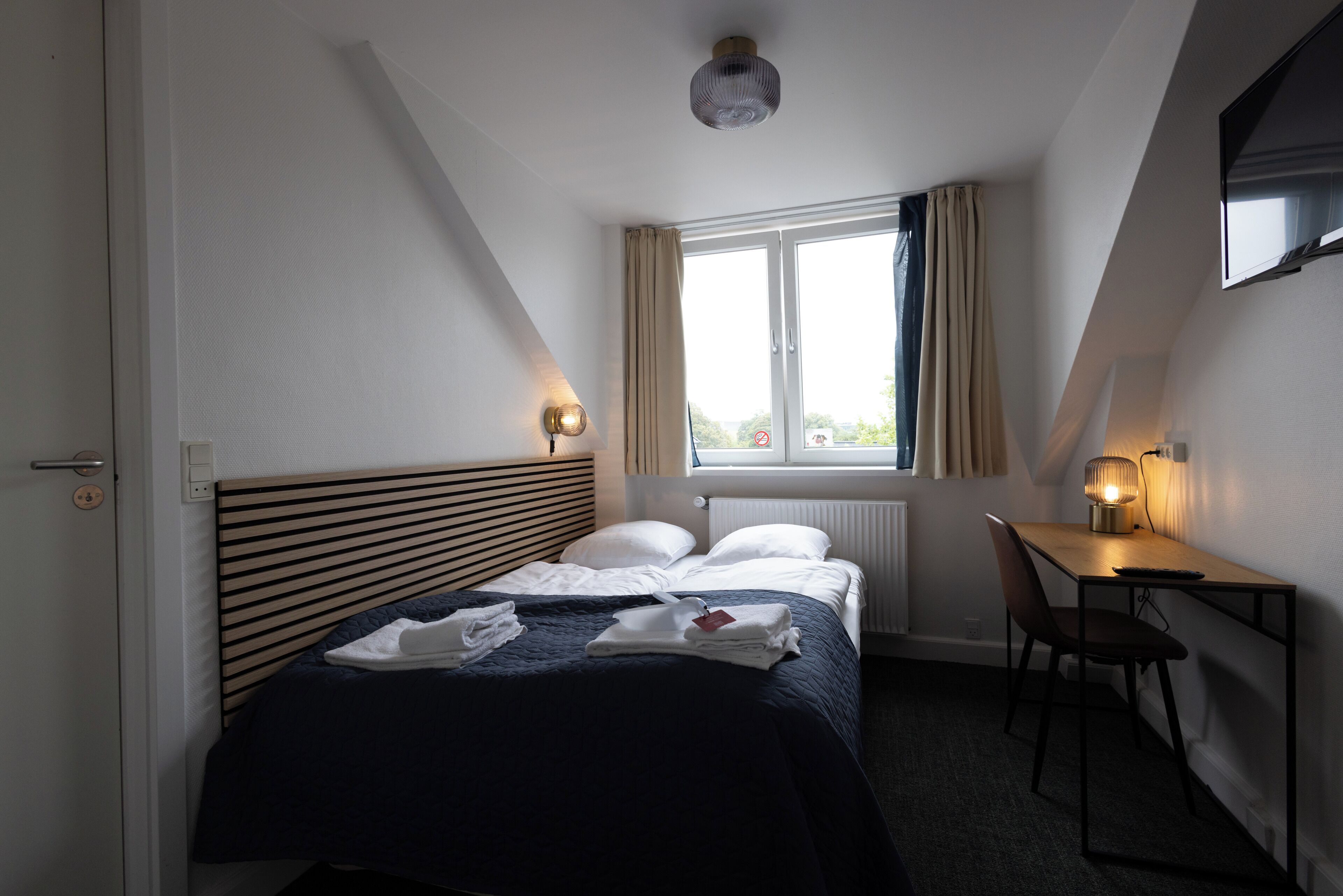 A bedroom with a bed, a desk, and a window with curtains.