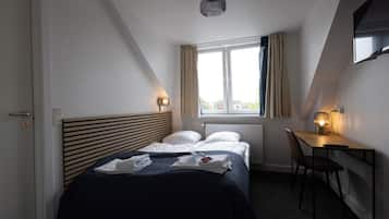 A bedroom with a bed, a desk, and a window with curtains.